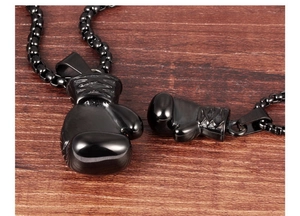Close-up of black stainless steel boxing glove pendants on a dark wood texture surface
