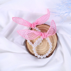 Detail of pink plaid bow hair ties with faux pearls on a minimalist wooden display