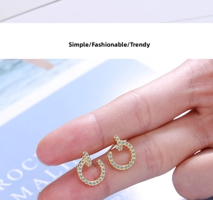 Close-up of hand holding a C-shaped gold stud earring with pavé white zircons