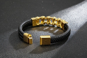 Detail of black braided leather bracelet with gold chain accents and magnetic clasp