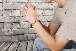 Detail of men's gold chain bracelet with black braided leather on a male model's wrist