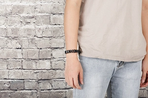 Detail view of a black braided leather bracelet with stainless steel geometric links on wrist