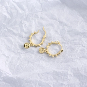 Detail of gold S925 sterling silver hoop earrings with sunburst coin charms on white paper
