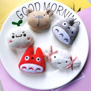 Selection of five cute cartoon plush pins and embroidery patches on a ceramic plate