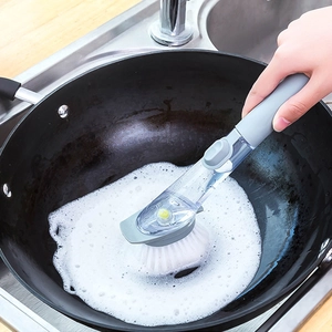 Long handle dish brush with soap dispenser scrubbing a black frying pan in a kitchen