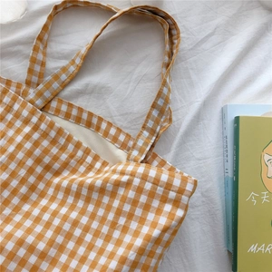 Detail view of the yellow plaid canvas tote bag with woven handles on white fabric