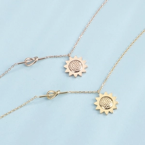 Colliers tournesol en acier inoxydable or rose et doré avec détail de nœud sur fond bleu