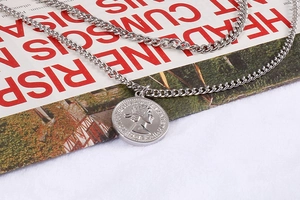 Dettaglio di catene cubane argentate a strati con pendente a moneta su una rivista