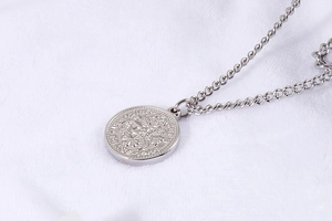 Dettaglio di collana argentata a strati con ciondolo moneta e rilievo su pelliccia bianca