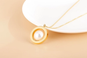 Détail d'un pendentif cercle doré avec perle blanche posé sur une assiette en porcelaine