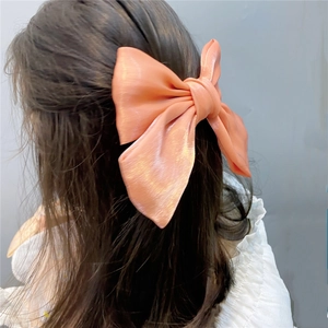Detail of a large coral pink satin bow hair clip worn by a model in a French style