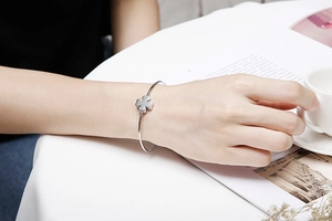 Close-up of a silver four-leaf clover adjustable bangle worn by a model holding a cup