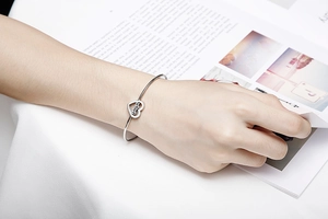 Close-up of silver heart bracelet with mama engraving on a model's wrist with magazine