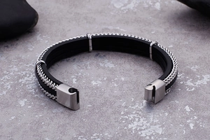 Detail of multi-layer woven black leather and steel bracelet with a square metal clasp