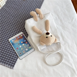 Détail d'un sac cabas en toile blanche avec un ours en peluche beige sur un drap blanc