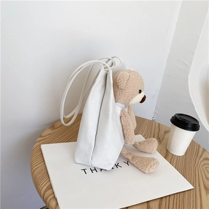 Détail du sac cabas en toile blanche avec un pendentif ours en peluche beige sur une table