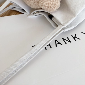 Détail d'un sac cabas en toile blanche avec ornement en polaire beige et fermoir magnétique