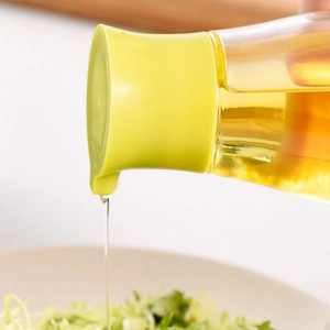 Distributeur d'huile en verre étanche avec couvercle vert versant sur une salade