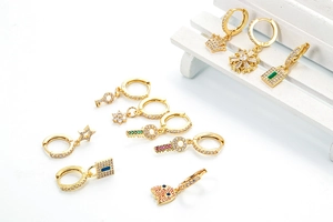 Nahaufnahme von goldenen Creolen mit Zirkonia-Schlüssel- und Sternanhängern im Detail