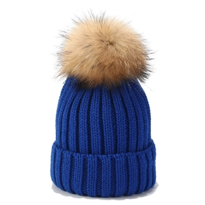 Detalle del gorro de punto azul real con pompón de piel de mapache marrón en la parte