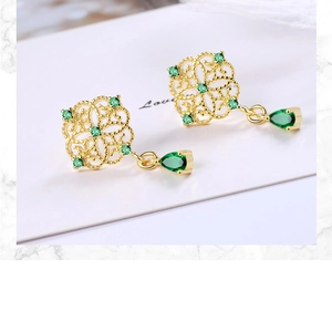 Close-up of vintage gold earrings with hollow patterns and emerald water-drop pendants