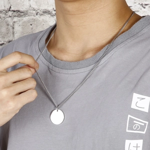 Collana minimalista con ciondolo tondo argento indossata da modella su sfondo di mattoni