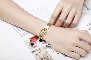 Détail du bracelet en maille dorée avec pendentif ancre en strass sur fond de magazine