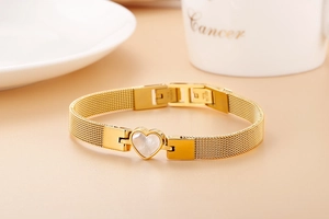 Detail of gold heart bracelet with white shell inlay and milanese mesh watch band strap