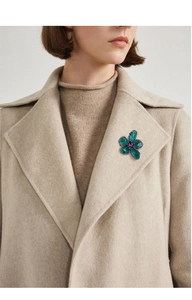 Close-up of vintage emerald crystal flower brooch pinned on a beige coat lapel