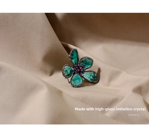 Detail of green crystal petals and purple rhinestone core on retro flower brooch