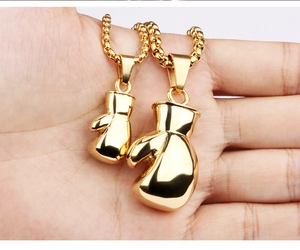 Close-up of gold stainless steel boxing glove pendants on pearl chains worn by a model