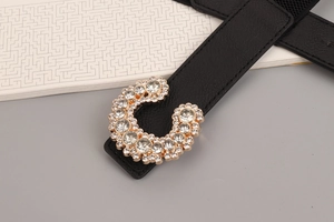 Close-up of golden C-shaped buckle with sparkling rhinestones on black elastic belt