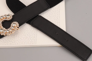 Detail of black elastic belt with gold C-shaped buckle encrusted with crystals