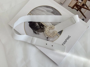 Detail of white elastic waist belt with sparkling C-letter rhinestone buckle on a magazine