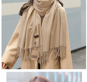 Detail of khaki cashmere scarf with tassels and ZHYING brand tag on a neutral coat