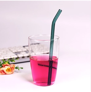 Detail of dark green bent glass straw in a drink with keyboard and pink flower