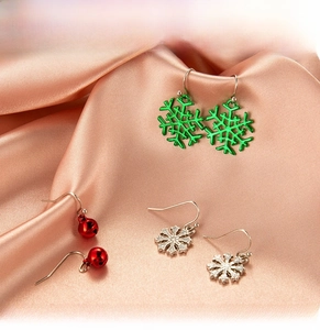 Detailed view of Christmas tree earrings with snowflakes and bells on pink satin