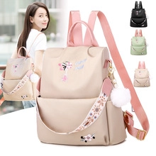 Detail of beige nylon backpack featuring floral embroidery and white fluffy ball pendant