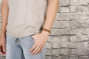 Close-up of golden geometric link bracelet worn on a wrist against a brick wall