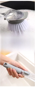 Detail of soap dispensing dish brush with non-slip handle and nylon bristles in action