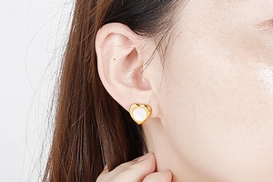 Close-up of heart-shaped gold earrings with white shell inlay worn by a female model