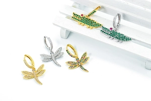 Detailed macro view of crystal-encrusted green crocodile and dragonfly drop earrings