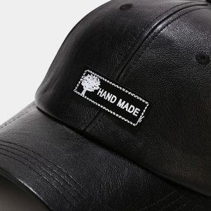 Close-up of black PU leather baseball cap featuring textured lychee grain and Hand Made tag