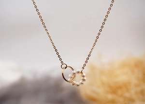 Macro shot of interlocking gold and micro-pearl rings on a delicate chain necklace