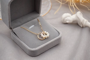 Macro view of 18K gold circle necklace with freshwater pearls on a grey velvet box