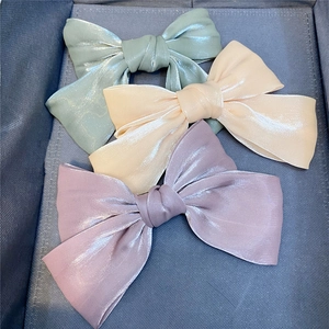 Close-up of three large satin bow hair clips in lavender, cream, and mint colors