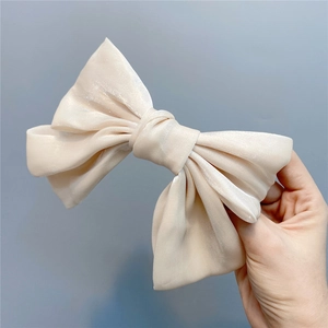 Detail showing the cream silk texture and large bow hair clip held by hand