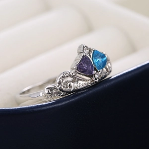 Elegant crown shaped silver ring with blue and purple heart stones on jewelry box