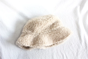 Texture detail of cream beige fuzzy lamb wool bucket hat on soft white linen background