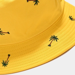 Macro view of detailed palm tree embroidery and fine stitching on a yellow cotton bucket hat
